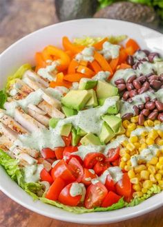 a salad with chicken, lettuce, tomatoes, corn and avocado