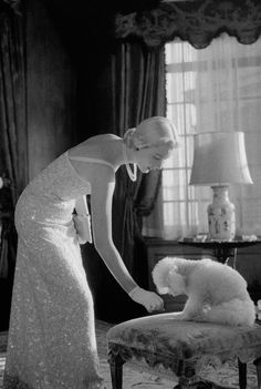 a woman in a dress petting a poodle on the foot of a chair