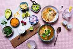 a table topped with bowls of food next to glasses and utensils on top of a pink cloth