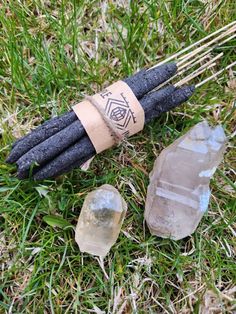 three crystal wands are on the grass with some stick wrapped around them, and one is black