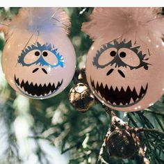 two ornaments hanging from a christmas tree decorated with cartoon faces and eyes, one is pink and the other is blue