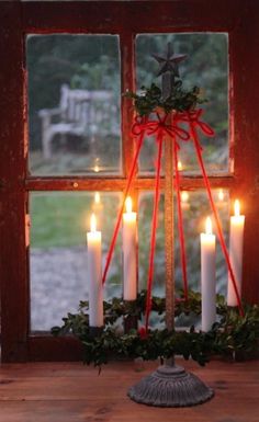 a candle holder with candles in front of a window decorated with holly and red ribbon