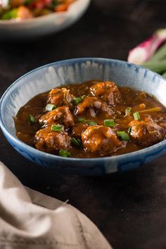 a blue bowl filled with meat covered in gravy and garnished with green onions