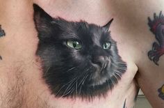 a black cat with green eyes is on the side of a man's chest