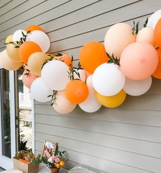 an orange and white balloon garland hanging from the side of a house