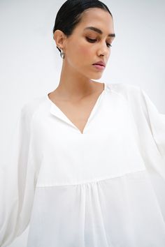 Our Kissena Top is your escape to a world of polished ease. A babydoll silhouette from lightweight European cotton voile, this billowing beauty features a notched neckline and raglan sleeves that flow down the arm before gathering into a cuff. Precisely tailored for effortless outfitting, Kissena is a refreshing take on a versatile daily essential. | Astrid, in off white, is 5'9" (175 cm) tall, wearing size XS. Yada, in black, is 5'9" (175 cm) tall, wearing size XS. Total length from the front i White Billowy Blouse For Summer, Billowy White Blouse For Summer, Billowy White Summer Blouse, White Flowy Breezy Blouse, Breezy Flowy White Top, Flowy Breezy Tops For Daywear, Flowy Summer Blouse For Daywear, Effortless White Blouse For Daywear, Effortless White Summer Blouse