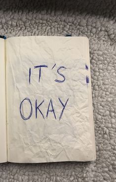 an open book with the words it's okay written in blue ink on white paper