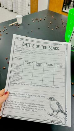 a person holding up a battle of the beaks paper in front of a table