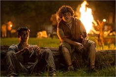 two young men sitting next to each other in front of a fire