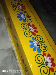 a yellow bench with colorful flowers painted on the top and bottom, along with tile flooring