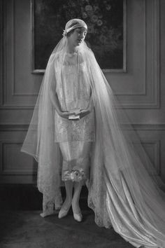 an old photo of a woman wearing a wedding dress and veil with her hands on her hips