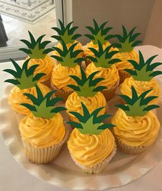 cupcakes with yellow frosting and pineapple decorations on a white platter