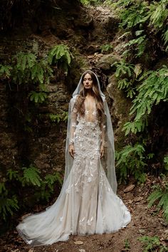 a woman wearing a wedding dress and veil standing in front of a waterfall with ferns