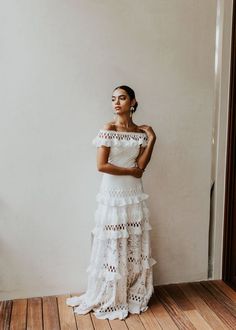 a woman standing in front of a white wall wearing a dress with tiered layers