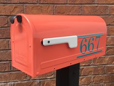 an orange mailbox with the number 667 on it is next to a brick wall