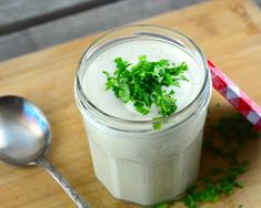 a glass filled with milk and parsley on top of a wooden cutting board next to a spoon