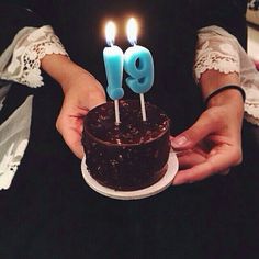 a woman holding a chocolate cake with lit candles