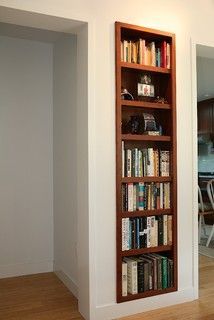 a bookshelf in the corner of a room with wooden floors and white walls