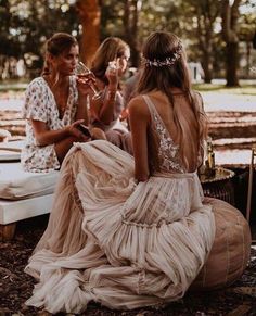 three women sitting on the ground talking to each other in front of an open fire pit