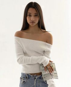 a woman in white shirt and jeans holding money with her hands behind her back while looking at the camera