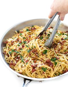 someone is using a fork to stir spaghetti in a pan with bacon and parsley