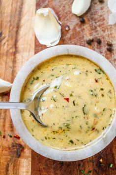 a white bowl filled with soup sitting on top of a wooden table next to garlic