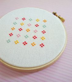 a cross stitch pattern is displayed on a white embroidery hoop with pink and yellow stripes