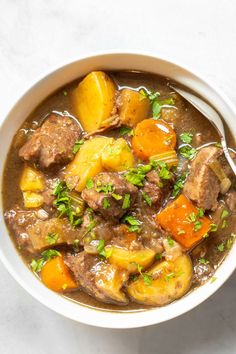 a white bowl filled with stew and potatoes on top of a table next to a spoon