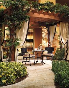 an outdoor dining area with table and chairs surrounded by greenery on either side of the patio