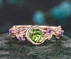 a ring with an oval green stone surrounded by purple stones on top of a rock