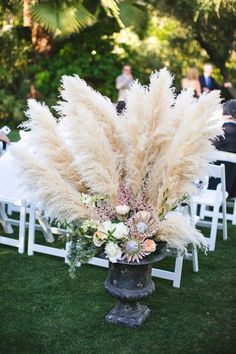 an arrangement of flowers and pamodia in a vase on the lawn at a wedding