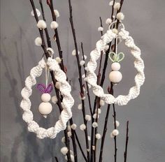 two white yarn wreaths are hanging from branches with balls and beads on them in front of a gray wall