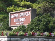 a sign for the eastern kentucky university campus in front of some trees and bushes with flowers around it