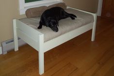 a large black dog laying on top of a white bed next to a wooden floor