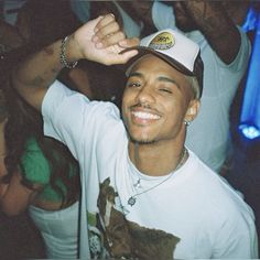 a man in a white shirt and hat at a party holding his hand up to the side