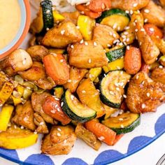 a blue and white plate topped with chicken and veggies next to a bowl of sauce