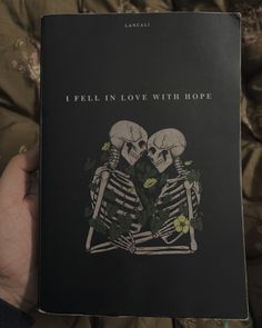 someone holding up a book that says i fell in love with hope and two skeletons