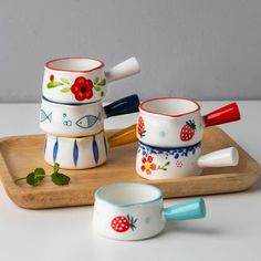 three ceramic bowls and spoons are sitting on a wooden tray, one is decorated with flowers