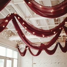 a room with red curtains and lights hanging from it's ceiling in front of a brick wall