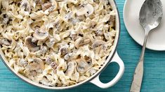 a casserole dish filled with pasta and mushrooms on a blue table cloth next to a white plate