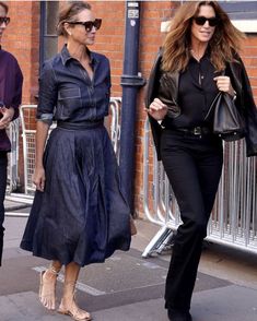 two women are walking down the street with one carrying a handbag and another wearing sunglasses