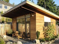 a small wooden building sitting in the middle of a yard with rocks and plants around it