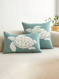 two pillows with sea turtles on them sitting on a couch next to a potted plant