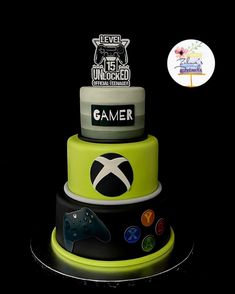 a three tiered cake with video game controllers on the top layer and an xbox sticker above it