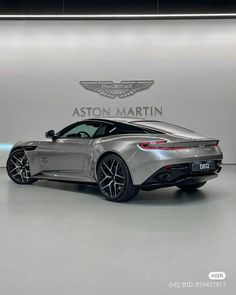 a silver sports car is parked in front of a wall with the words aston martin on it