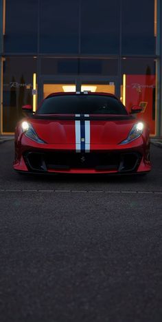 a red sports car is parked in front of a building at night with its lights on