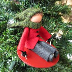 a red ornament hanging from a christmas tree with a green hat and coat