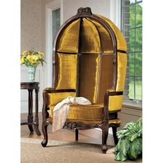 an ornate chair with yellow velvet upholstered back and seat, in front of a window