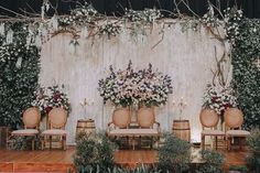 an outdoor wedding setup with chairs and flowers on the back wall, surrounded by greenery