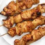 several skewers of chicken on a white plate